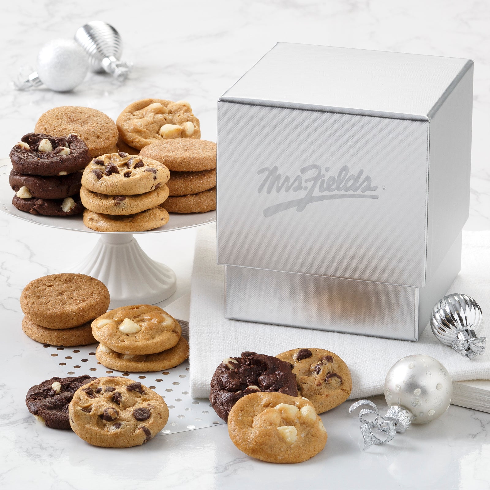A silver Mrs Field mini gift box surrounded by an assortment of Nibblers®