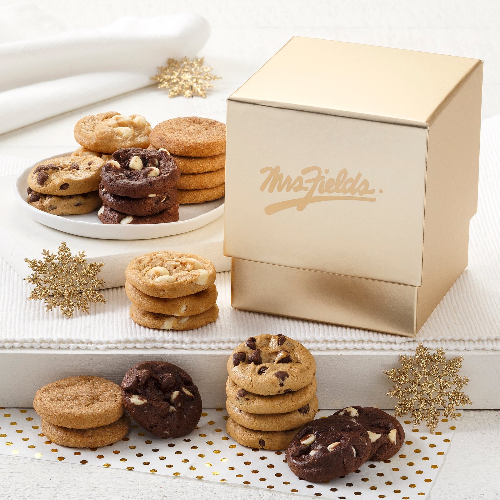 A gold Mrs. Fields mini gift box surrounded by an assortment of Nibblers®