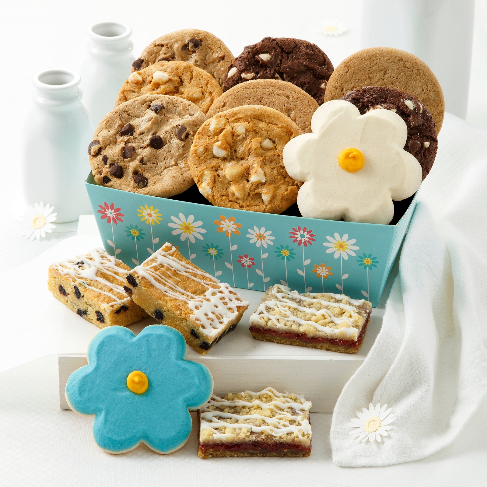 A blue flower crate filled with an assortment of original cookies and a white frosted flower cookie. Placed in front are an assortment of fruit bars and a blue frosted flower cookie.