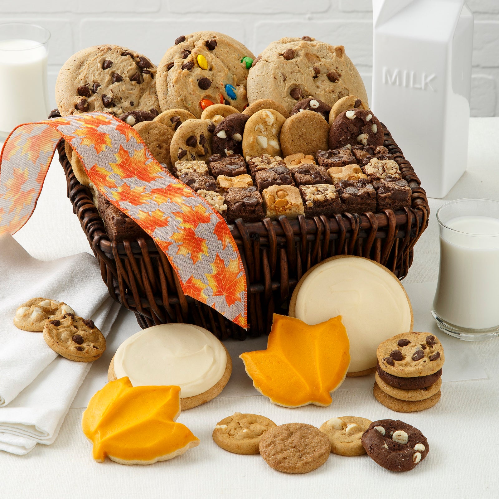 Small brown basket filled with mega cookies, Nibblers®, and brownie bites. In front of basket is an assortment of Nibblers®, two round frosted cookies and two leaf cookies.