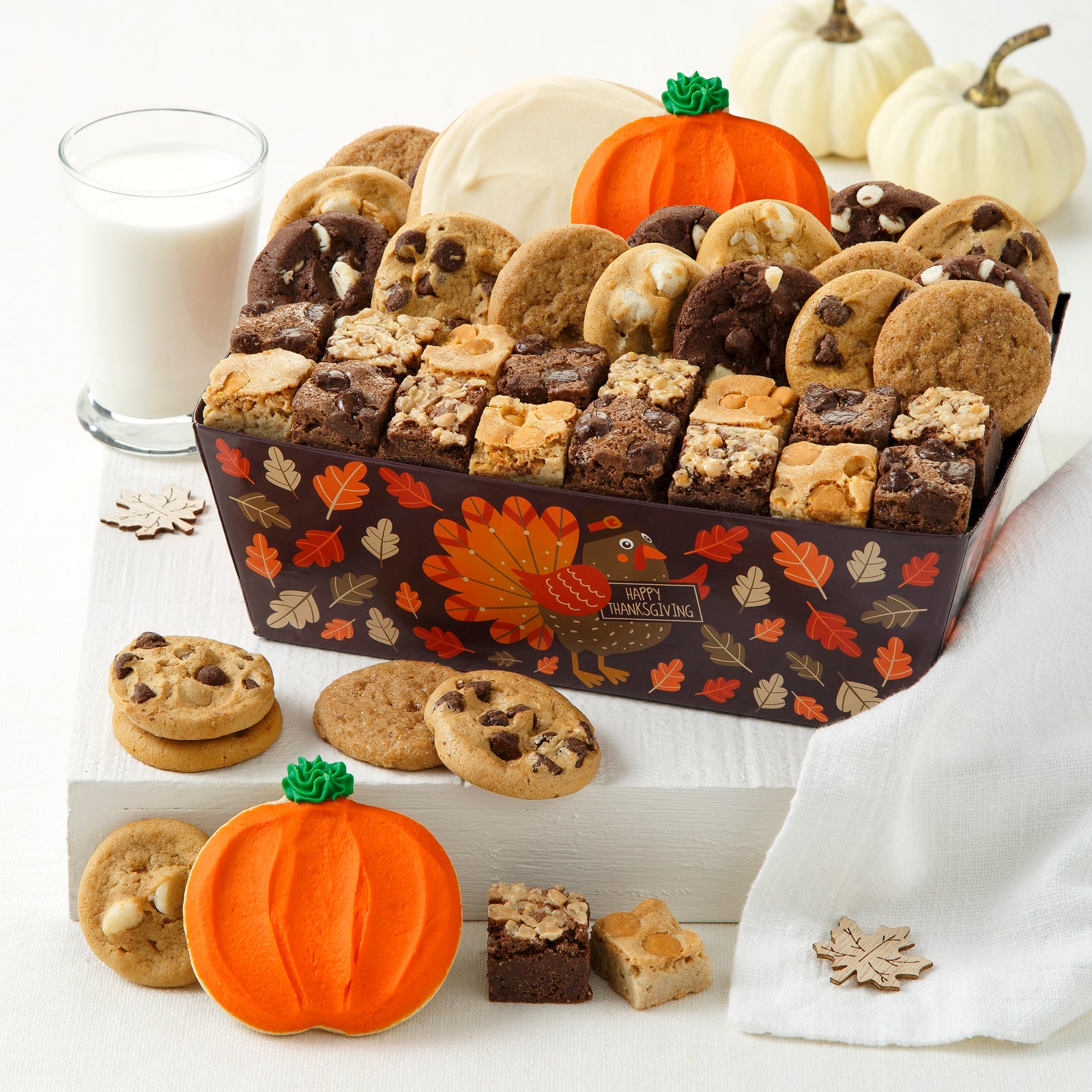 Brown Happy Thanksgiving crate filled with an assortment Nibblers®, brownie bites, and two frosted cookies. Laid out in front are an assortment of Nibblers® and a frosted pumpkins