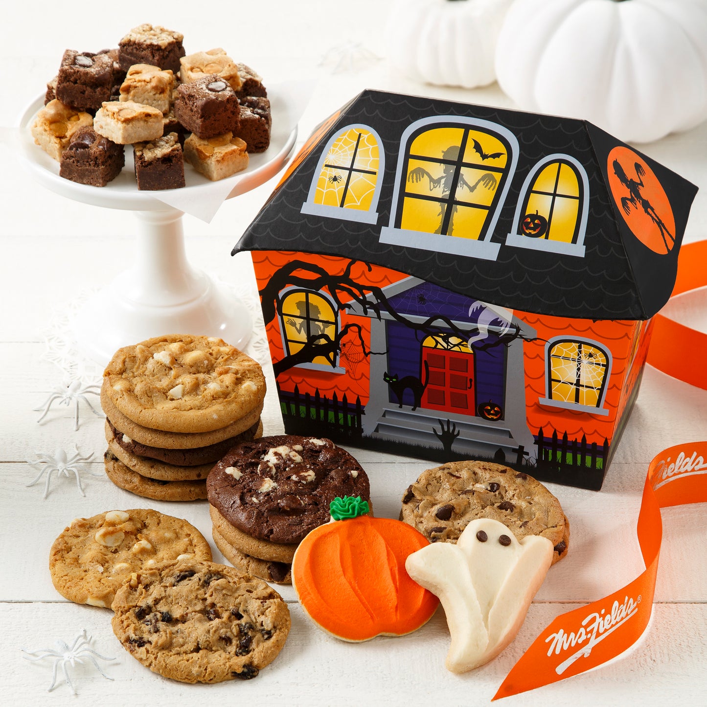 Haunted house themed cookie box. Surrounding this gift box is an assortment of brownie bites, original cookies, a frosted pumpkin cookie and a frosted ghosted cookie