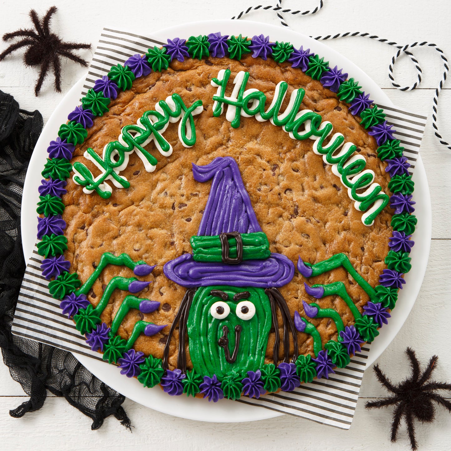 Halloween themed cookie cake with a Happy Halloween sentiment with a witch in green and purple frosting