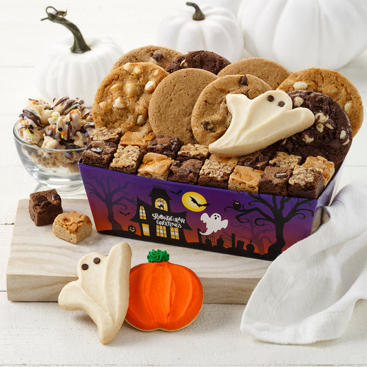 A Halloween themed crate with a spooky haunted house and filled with an assortment of original cookies, brownie bites, two frosted ghosts, and one frosted pumpkin cookie