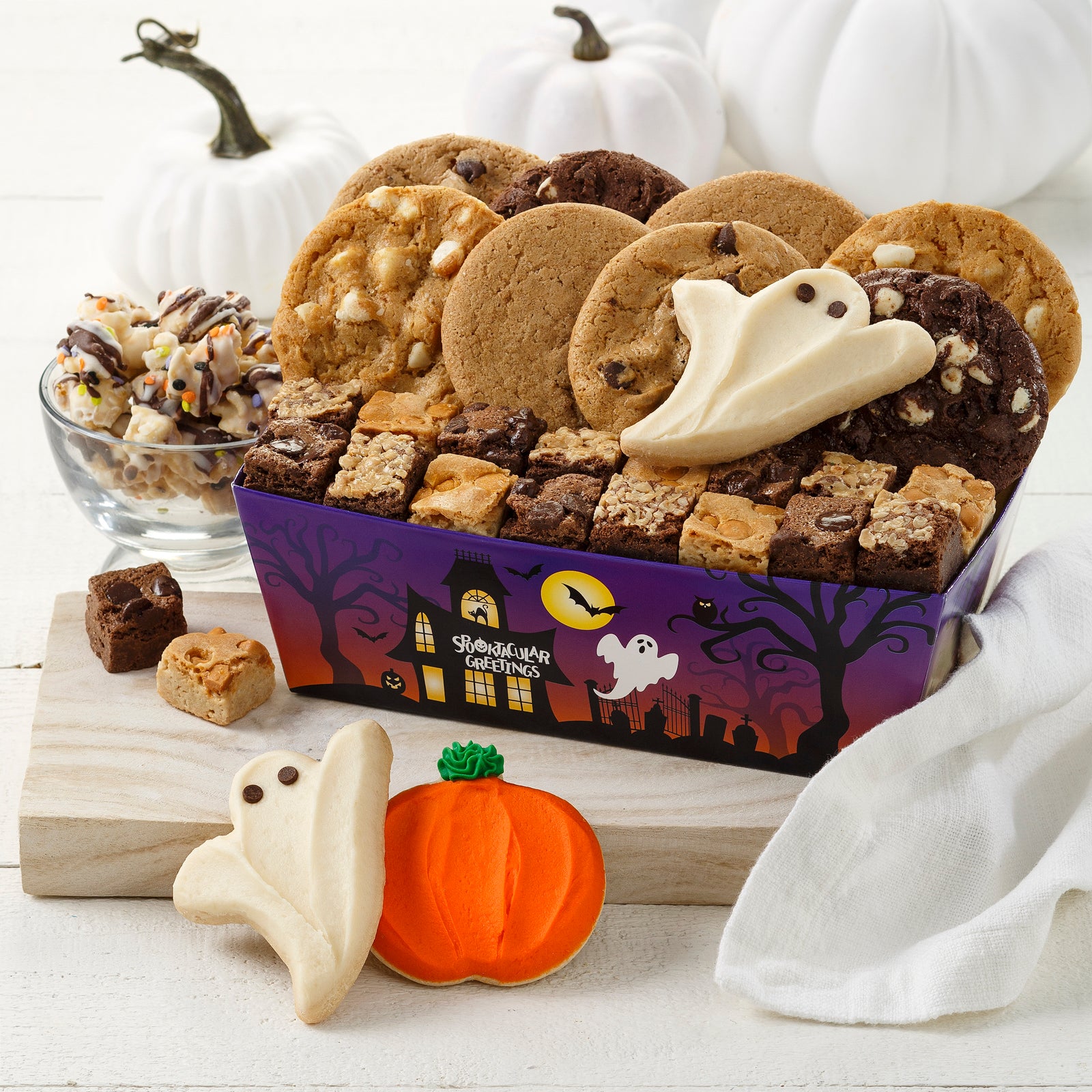 A Halloween themed crate with a spooky haunted house and filled with an assortment of original cookies, brownie bites, two frosted ghosts, and one frosted pumpkin cookie
