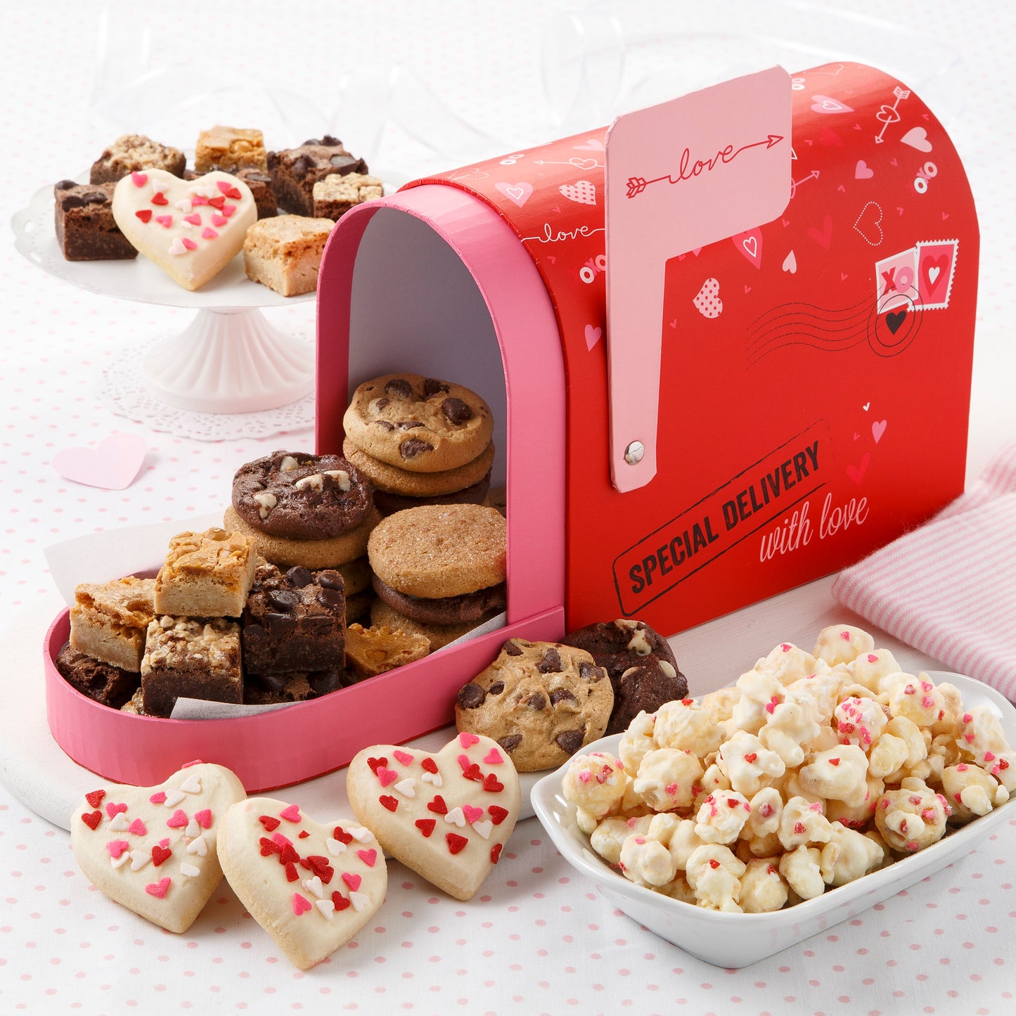 A mailbox themed for Valentine's Day gift box and filled with an assortment of Nibblers, brownie bites, 4 frosted mini heart cookies, and popcorn
