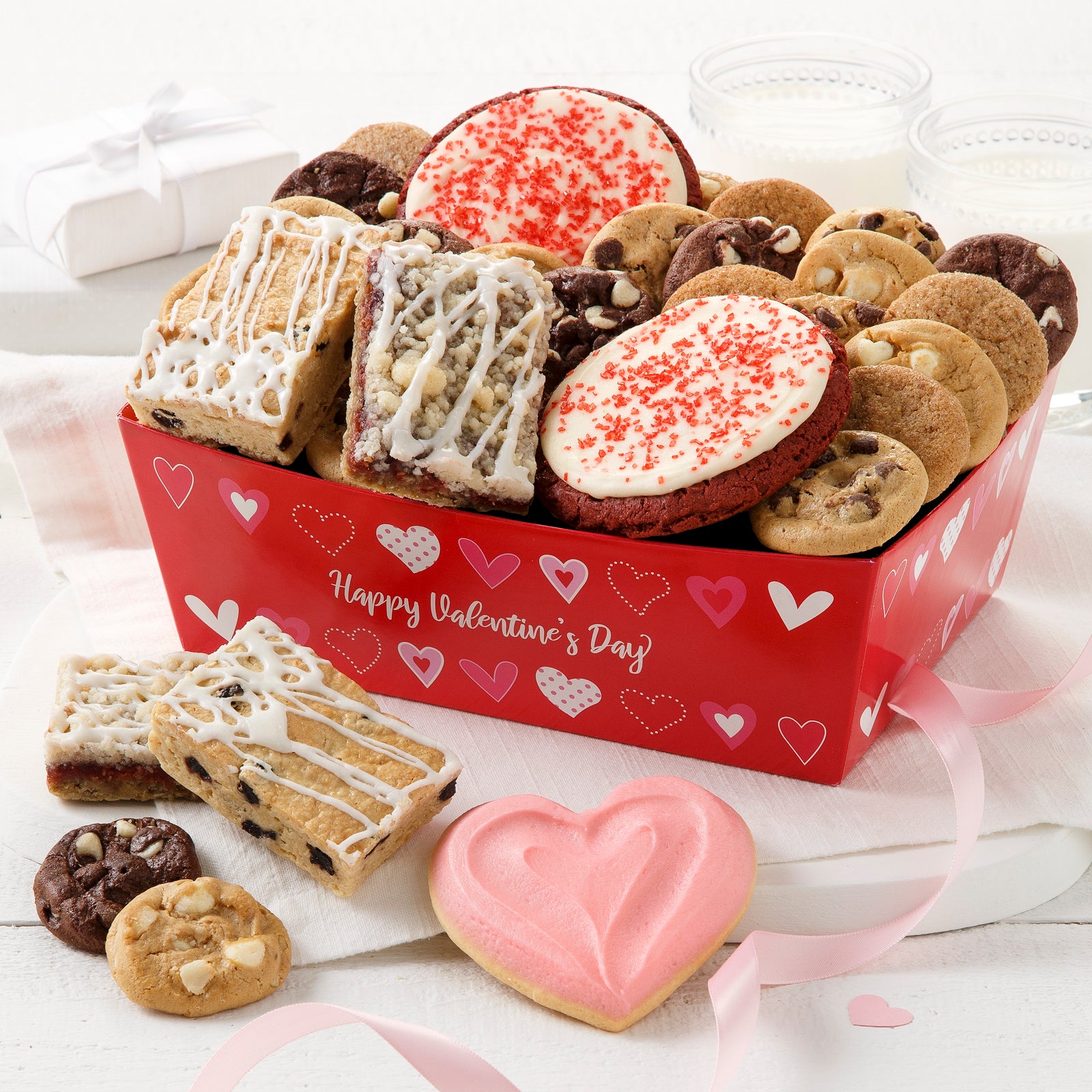 A red with hearts gift crate filled with an assortment of nibblers, fruit bars, two red velvet frosted cookies, and one frosted heart cookie