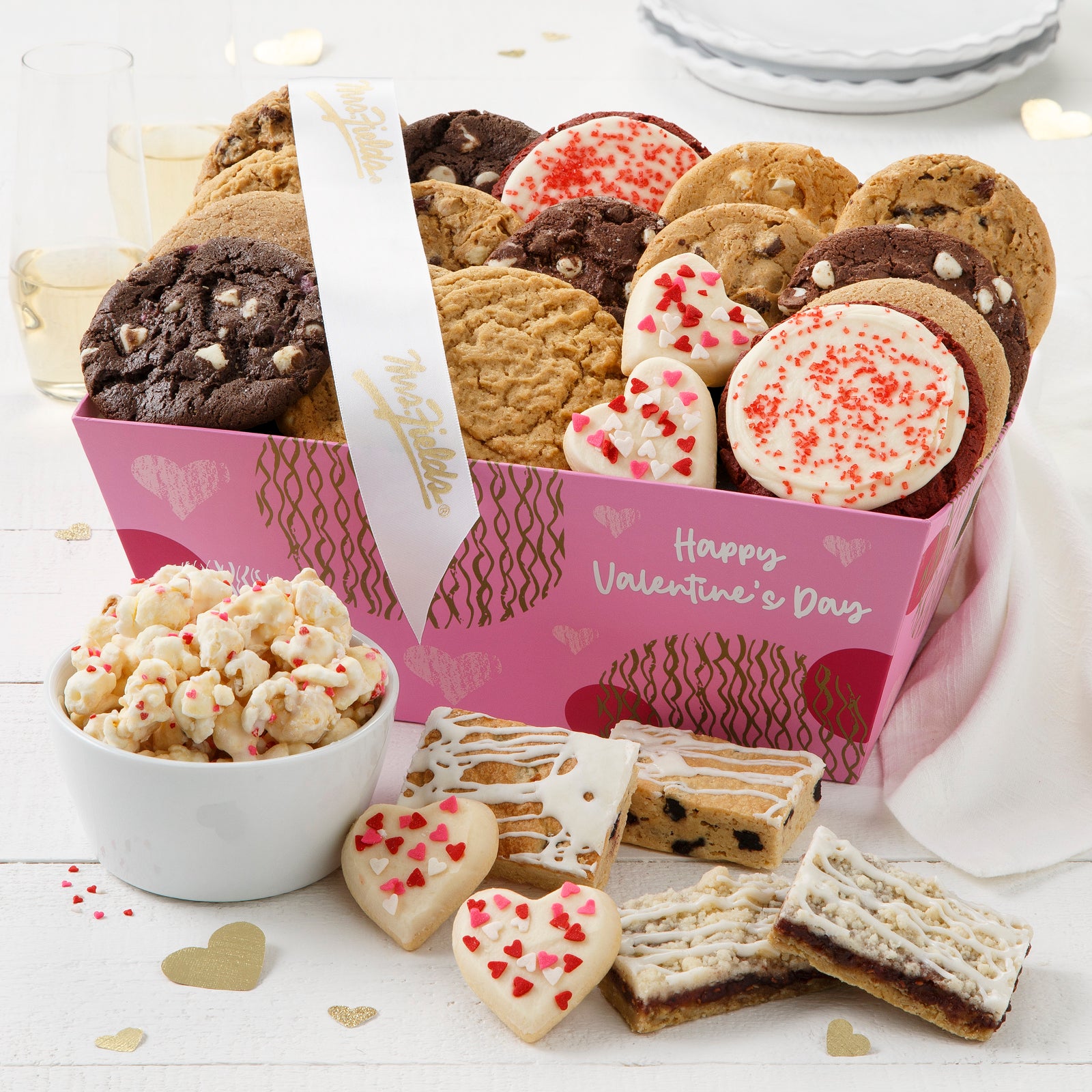 A pink Happy Valentine's Day crate filled with an assortment of original cookies, frosted red velvet frosted cookies, frosted mini heart cookies with sprinkles, fruit bars, and popcorn. 