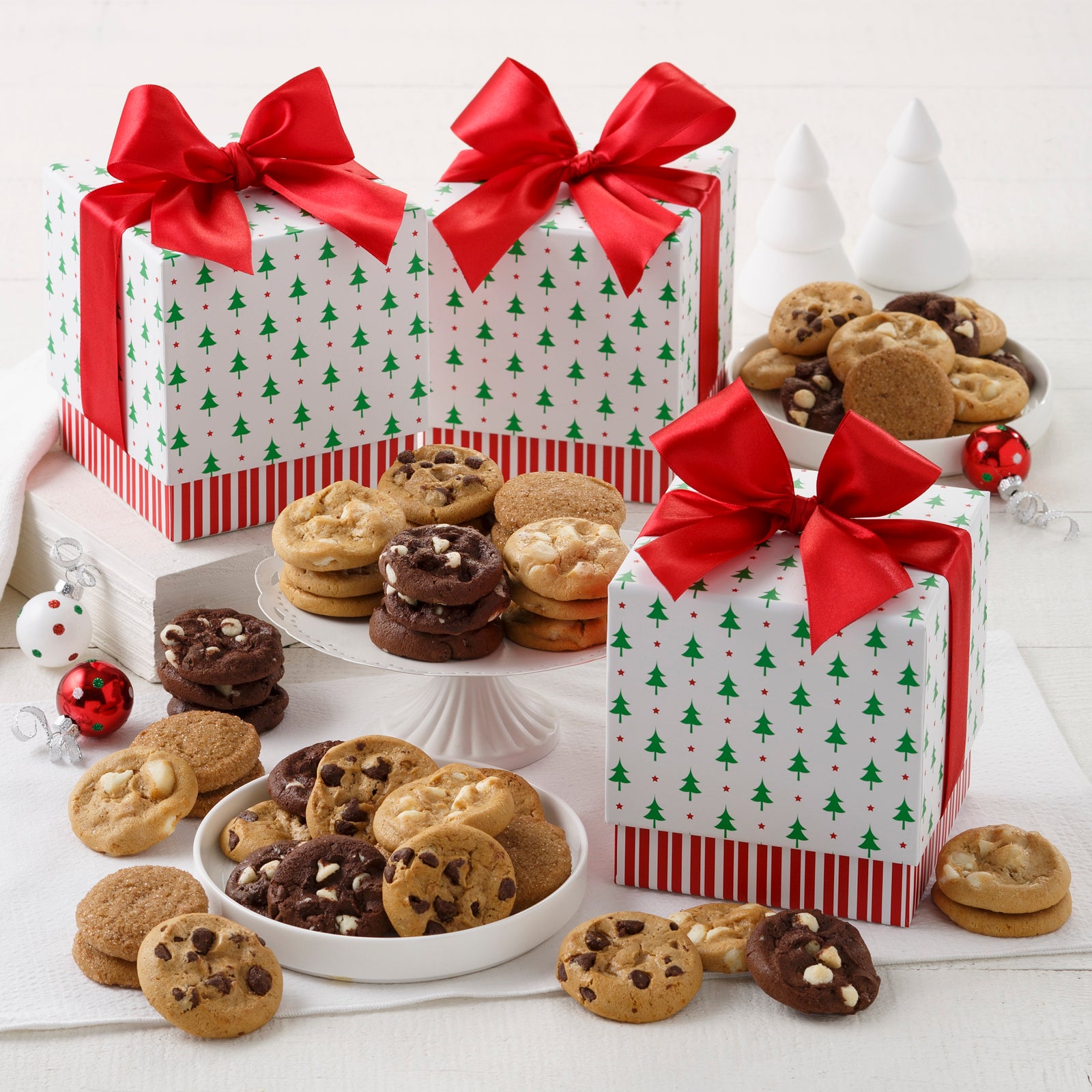 3 Mini gift boxes with Christmas trees on the top and a red and white striped base. There is an assortment of Nibblers® surrounding the gift box