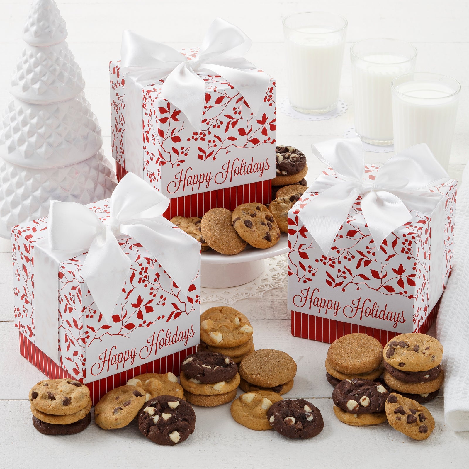 Three Happy Holidays mini gift boxes decorated with holly and surrounded by nut free Nibblers®