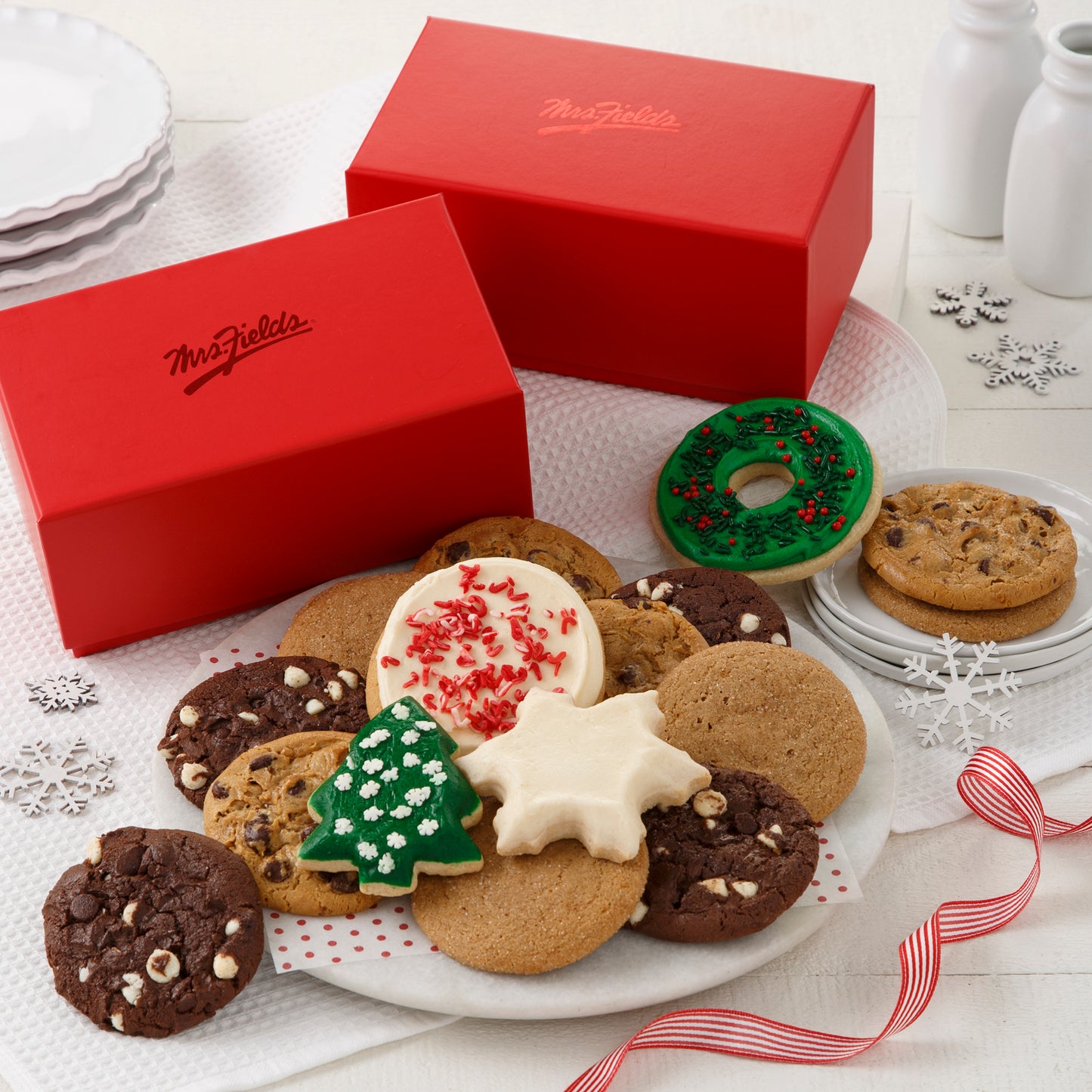 Two Mrs. Fields Cookie Trunks surrounded with an assortment of original cookies, a frosted wreath cookie with sprinkles, a frosted peppermint cookie with sprinkles, a frosted tree with sprinkles, and a frosted snowflake.