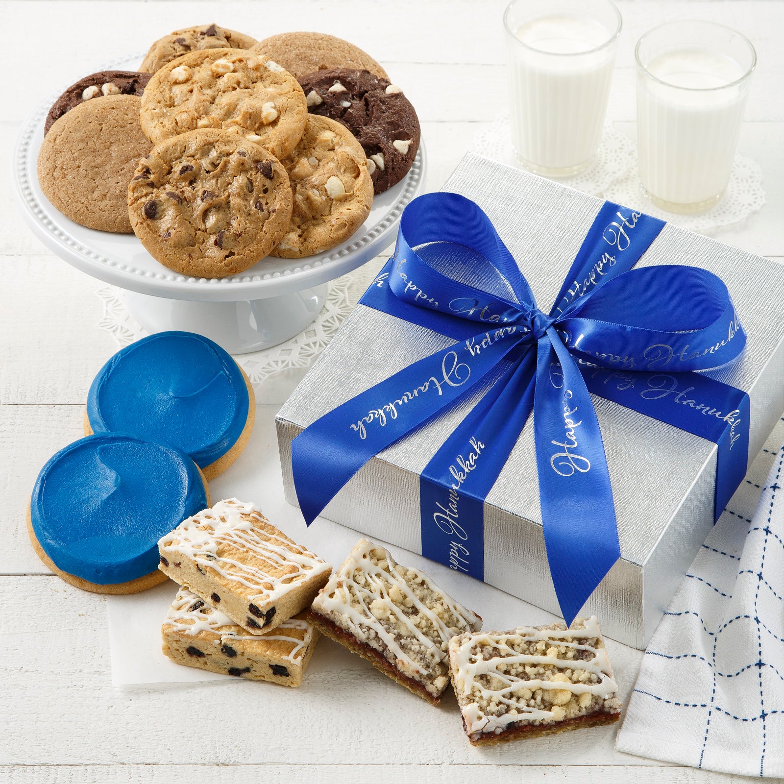 A silver gift box tied with a Happy Hanukkah blue and silver ribbon and surrounded by an assortment of original cookies, fruit bars, and two blue frosted cookies