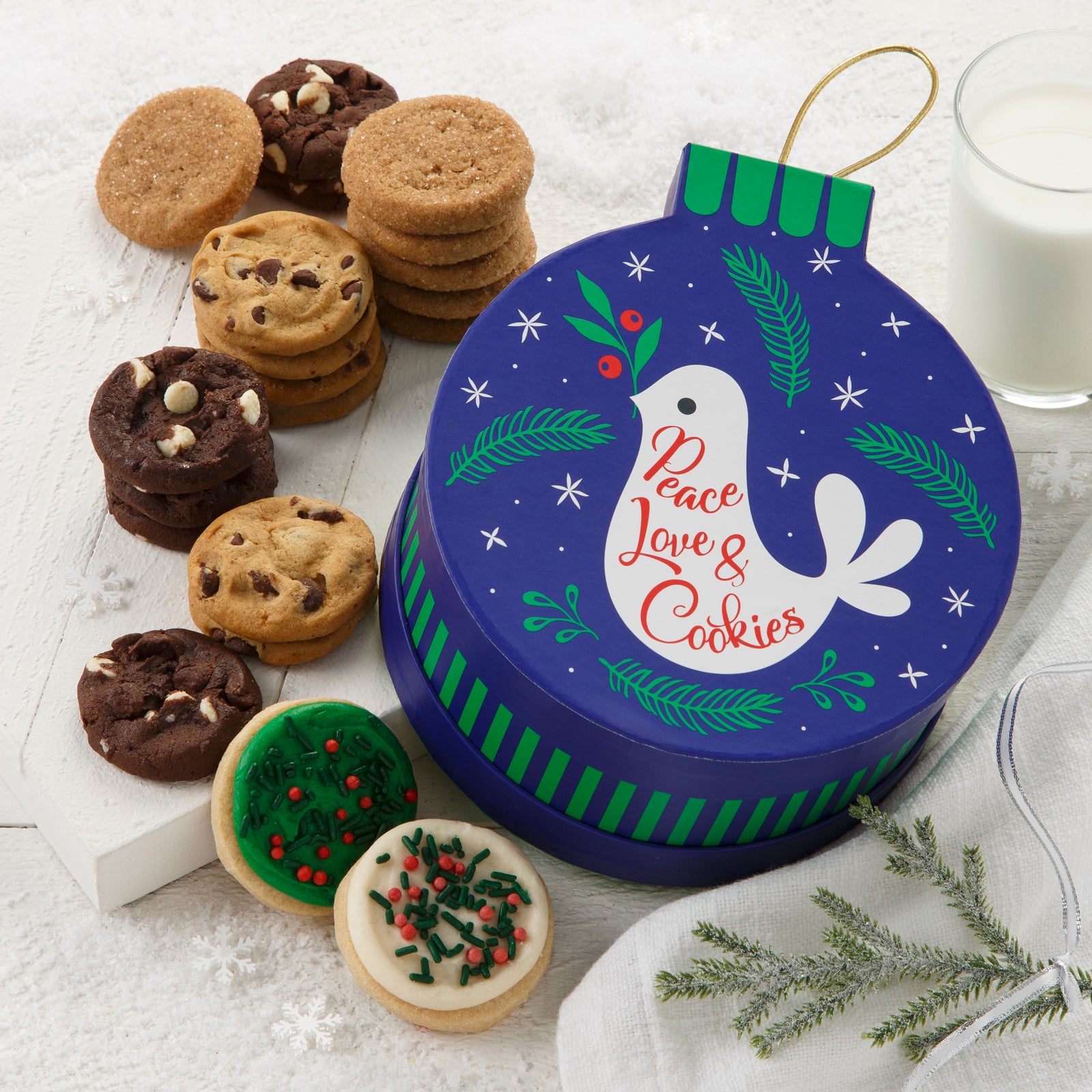 An ornament-shaped box decorated with a cute bird with the sentiment of Peace, Love, and Cookies and surrounded by an assortment of Nibblers® and two frosted mini cookies with sprinkles.