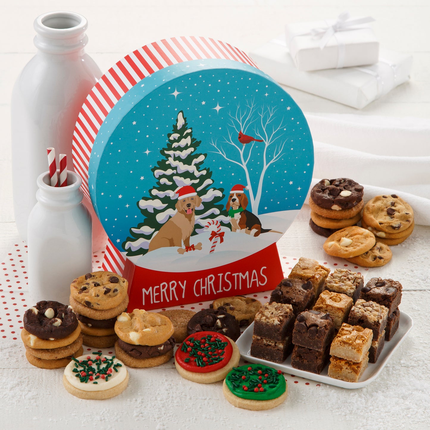 A snow globe-shaped gift box decorated with a winter scene of two dogs and a red cardinal bird and surrounded with an assortment of Nibblers®, brownie bites, and three frosted mini cookies with sprinkles.
