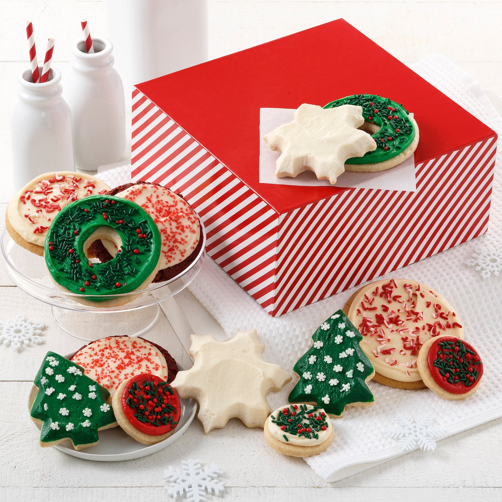 Red and white striped gift box surrounded by an assortment of holiday themed frosted cookies