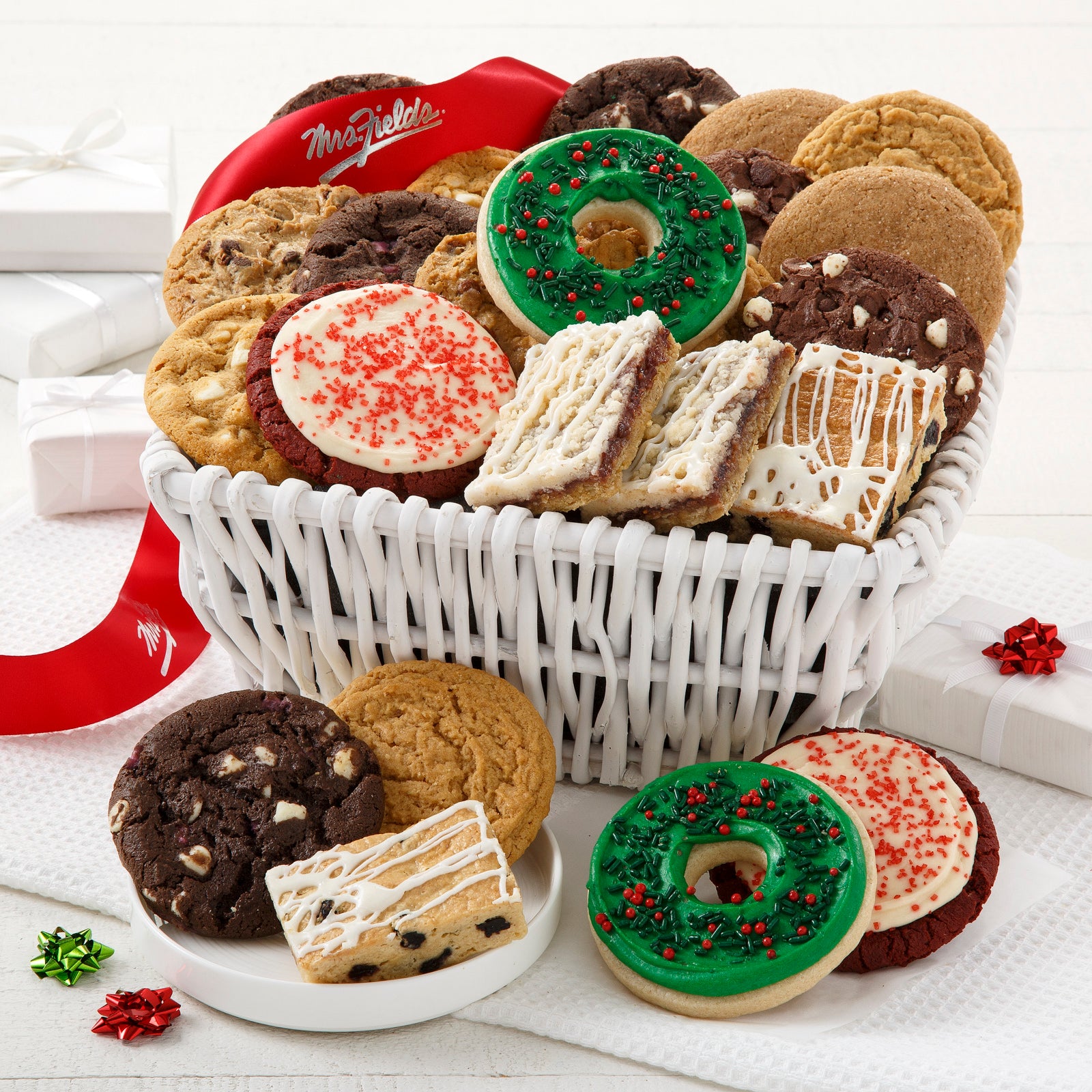 A white basket filled with an assortment of original cookies, four fruit bars, and four frosted cookies. tied with a red Mrs Fields ribbon