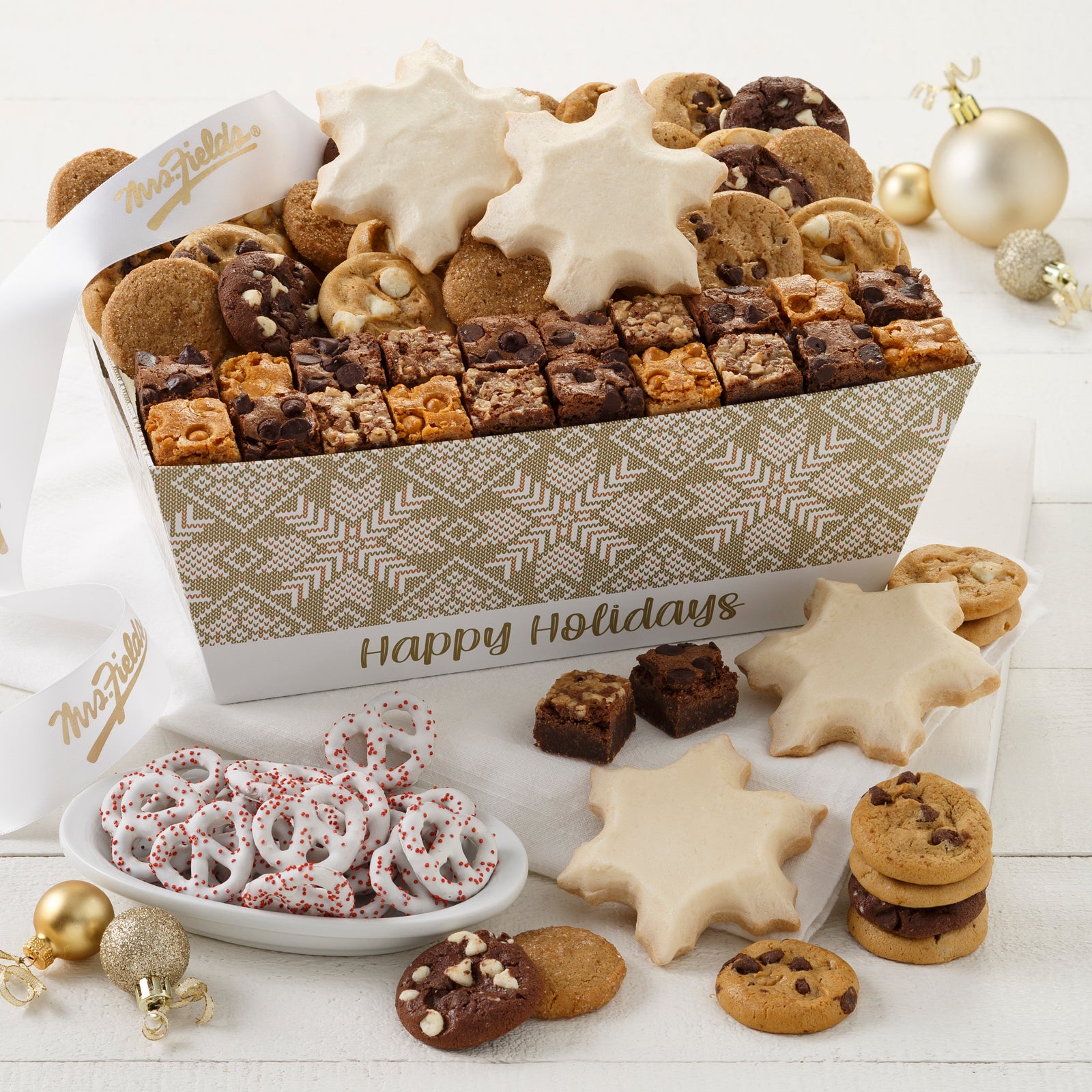 A Happy Holidays crate decorated with a gold and white holiday pattern and filled with an assortment of Nibblers®, brownie bites, four frosted snowflake cookies, and yogurt-covered pretzels.