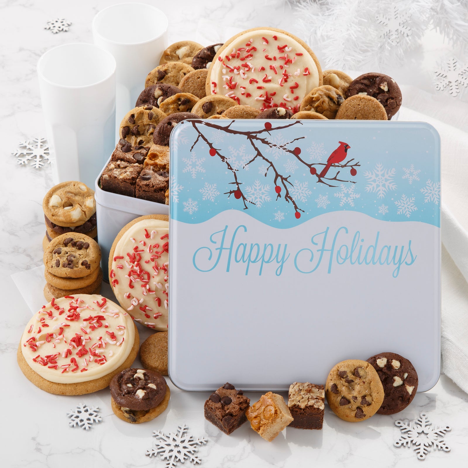 An outdoor winter scene with a red cardinal as decoration on a gift tin that is filled with an assortment of Nibblers®, brownie bites, three frosted peppermint cookies with sprinkles