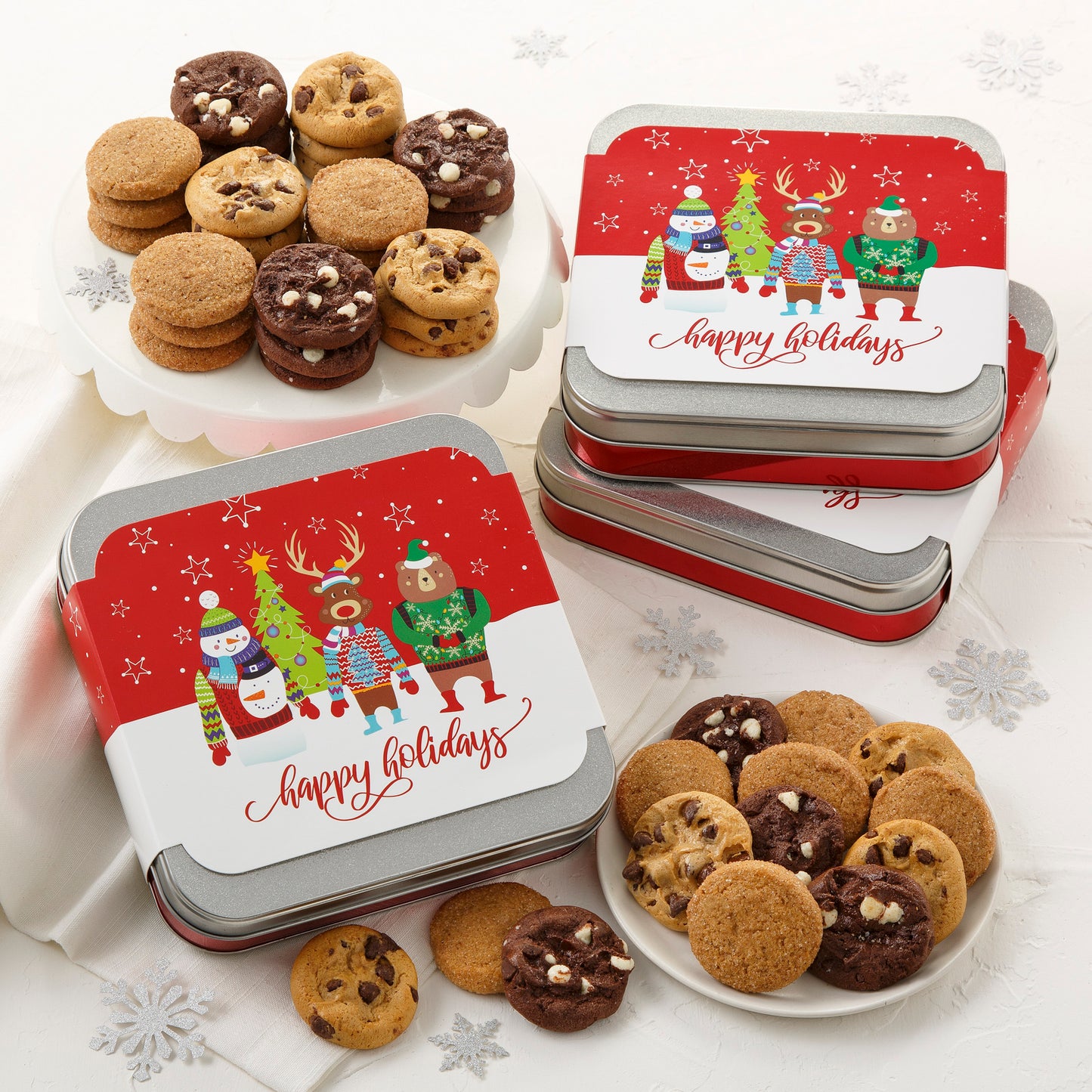 Three mini gift tins with a holiday-themed sleeve with fun woodland creatures on the top. These tins are surrounded by an assortment of Nibblers® bite-sized cookies