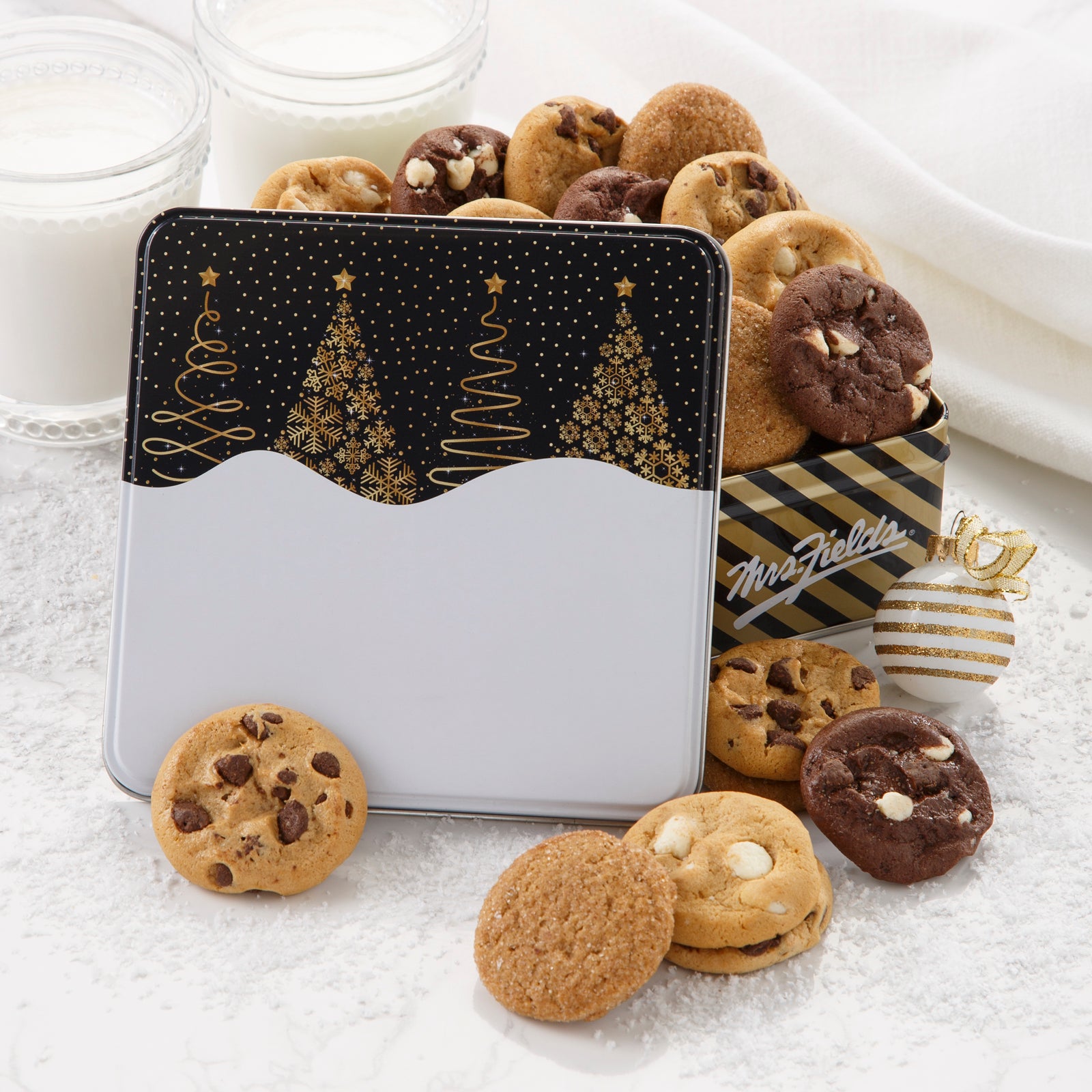A black and gold gift tin decorated with Christmas trees and filled with an assortment of Nibblers®