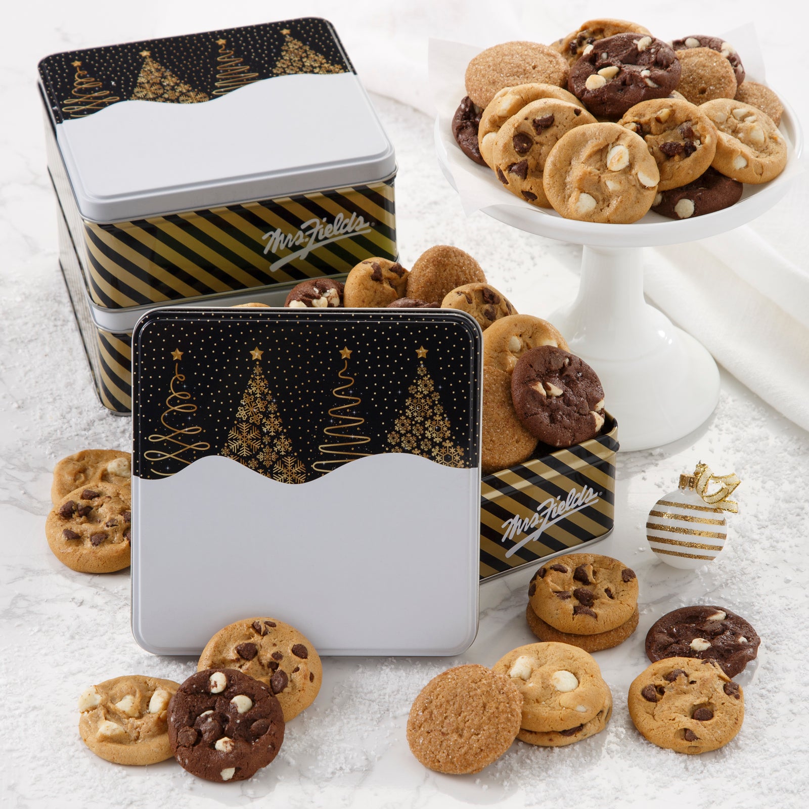 Three black and white holiday tins decorated with Christmas trees and filled with an assortment of Nibblers®