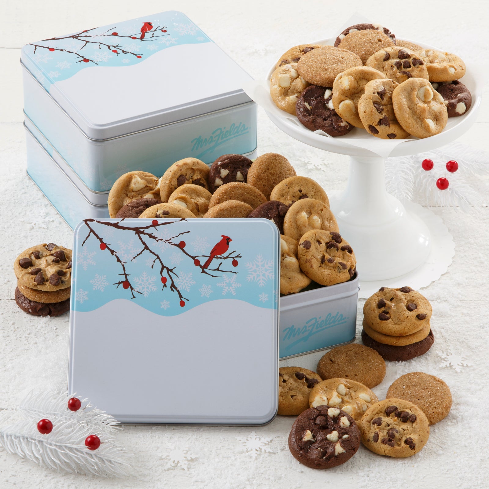 An outdoor winter scene with a red cardinal as decoration on a three gift tins that is filled with an assortment of Nibblers®
