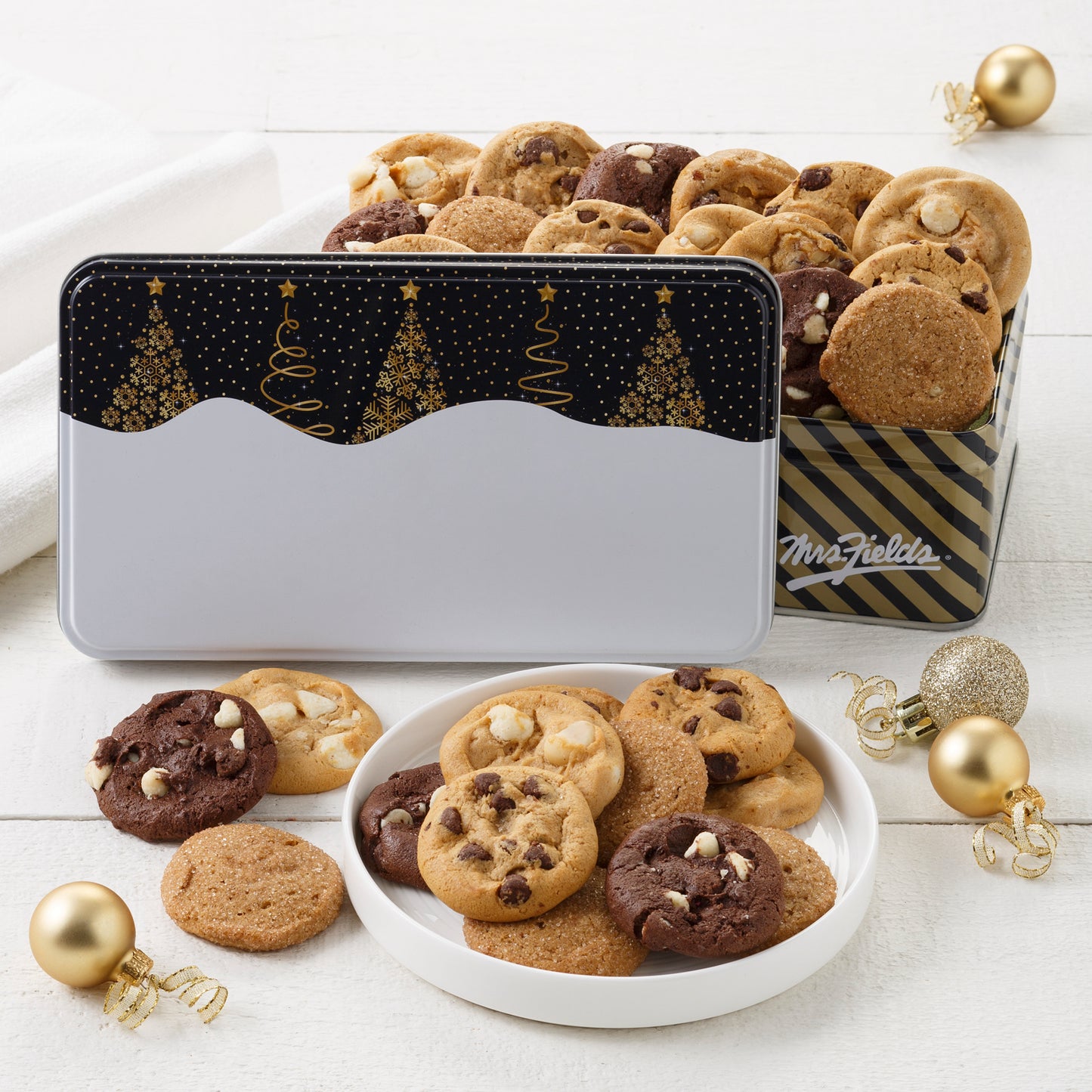 A black and white holiday tins decorated with Christmas trees and filled with an assortment of Nibblers®