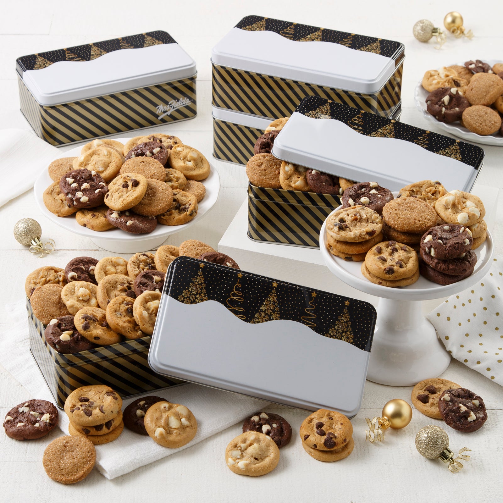 Four black and gold tins decorated with Christmas trees and filled with an assortment of Nibblers®