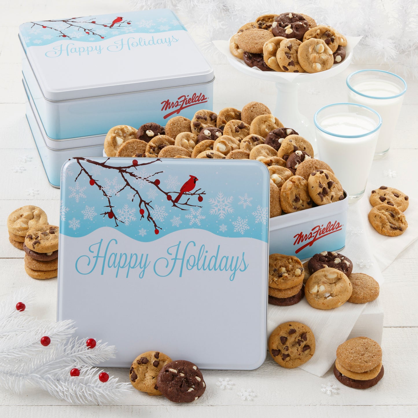 An outdoor winter scene with a red cardinal as decoration on three gift tins that are filled with an assortment of Nibblers®