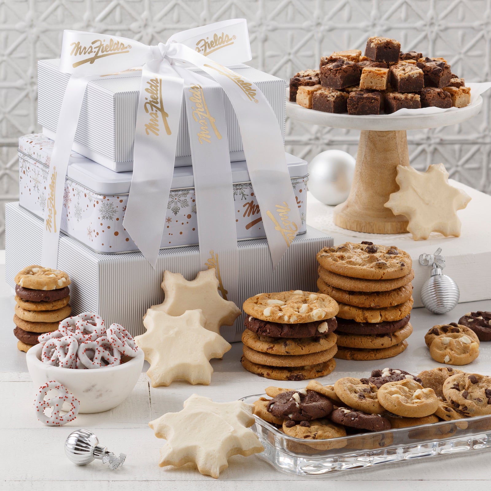 A white, gold, and silver three-tier tower surrounded by an assortment of original cookies, brownie bites, Nibblers®, four frosted snowflake cookies, and yogurt-covered pretzels.