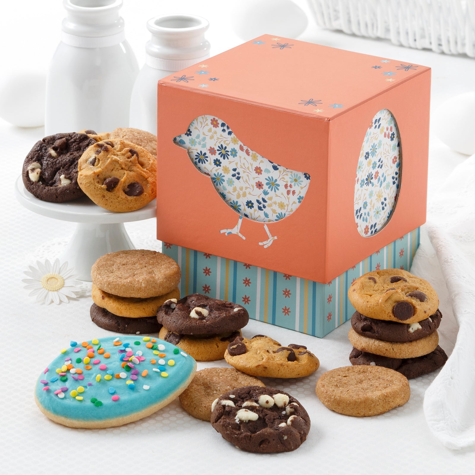 A coral and blue Easter themed mini gift box surrounded by an assortment of nibblers and a frosted egg cookie.
