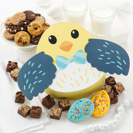 A chick gift box surrounded by an assortment of nibblers, brownie bites, and two frosted egg cookies