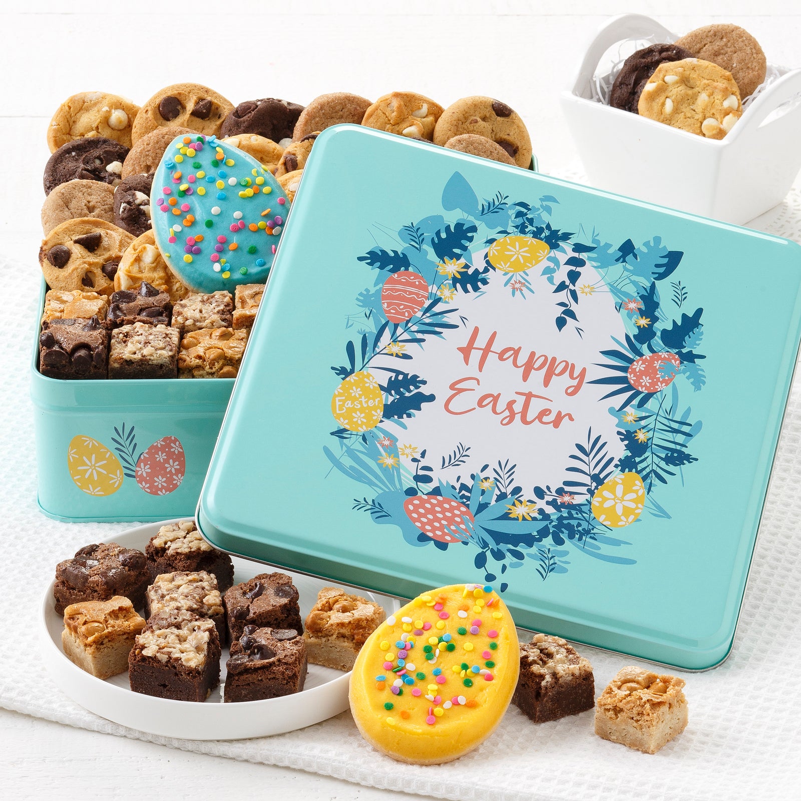 A light blue Easter themed gift tin with a Happy Easter sentiment and filled with an assortment of nibblers, brownie bites, and frosted egg cookies