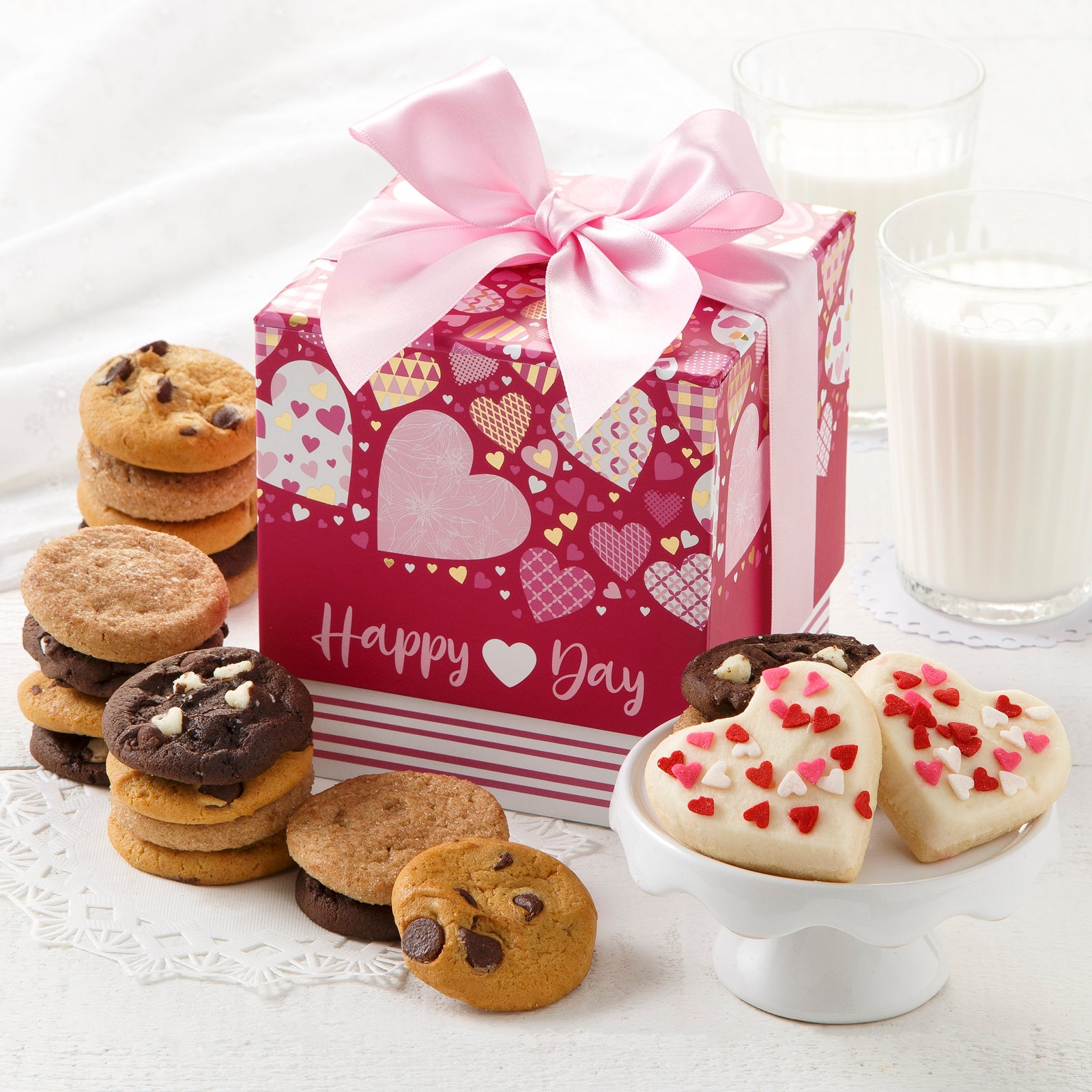 A mini Happy Valentine's Day gift box decorated with different size hearts and surrounded by an assortment of Nibblers and two mini frosted heart cookies with sprinkles