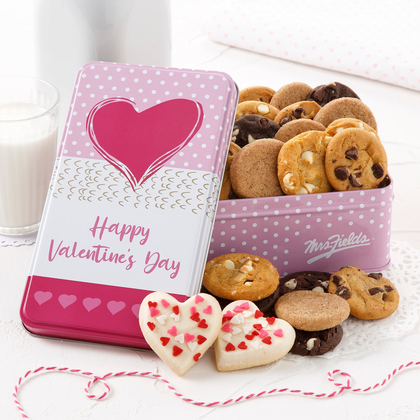 A pink Happy Valentine's Day gift tin filled with an assortment of Nibblers and two mini frosted heart cookies with sprinkles.