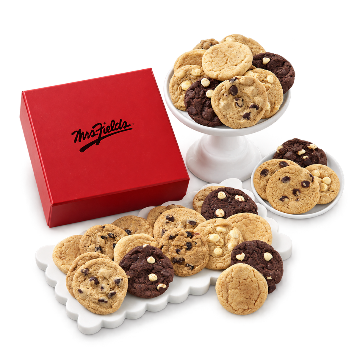 An assortment of chocolate chip cookies and chocolate cookies displayed on white pedestal stands and plates next to a red Mrs. Fiorellis gift box on a white background.