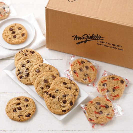 A large mailer box of Mrs. Field's chocolate chip cookies with several cookies displayed on a white plate and wrapped individually in Mrs. Fields printed wrapping on a white surface.