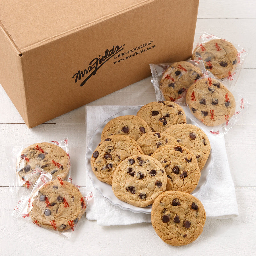A large mailer box of Mrs. Field's chocolate chip cookies with several cookies displayed on a white plate and wrapped individually in Mrs. Fields printed wrapping on a white surface.