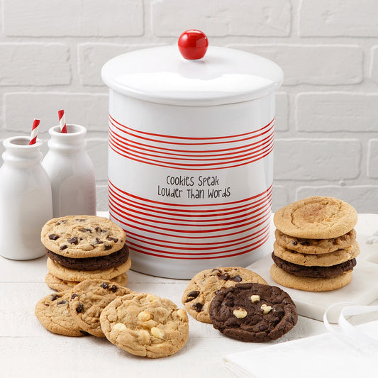 Ceramic cylindrical white and red cookie jar that says "cookies speak louder than words" on it surrounded by an assortment of fourteen Mrs. Fields original cookies.