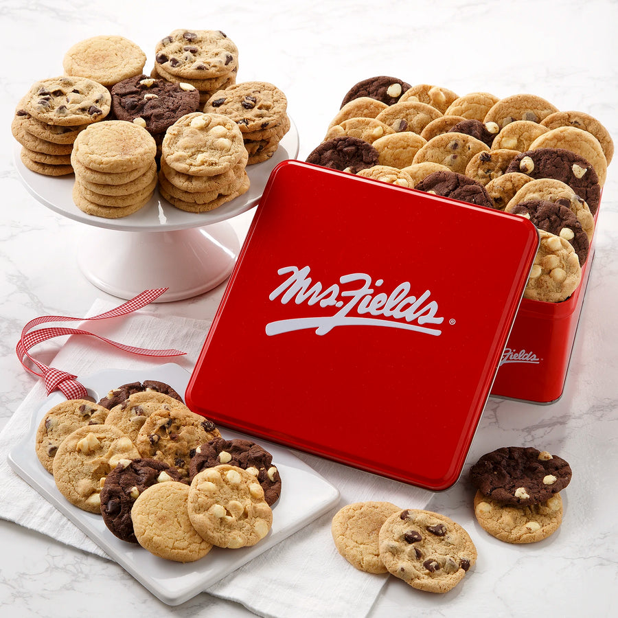 A red Mrs. Fields cookie tin filled with a large assortment of Nibblers bite-sized cookies on a white marbled surface.