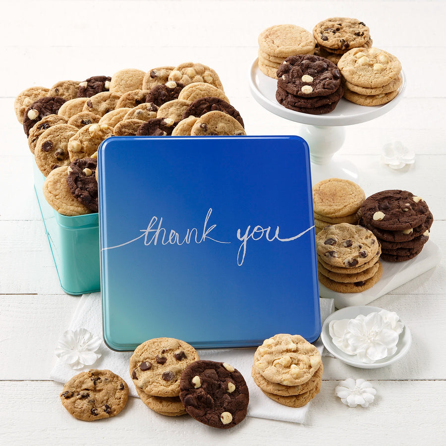 A blue hombre cookie tin that says "thank you" in a cursive font surrounded by an assortment of Nibblers bite-sized cookies on a white wooden surface.