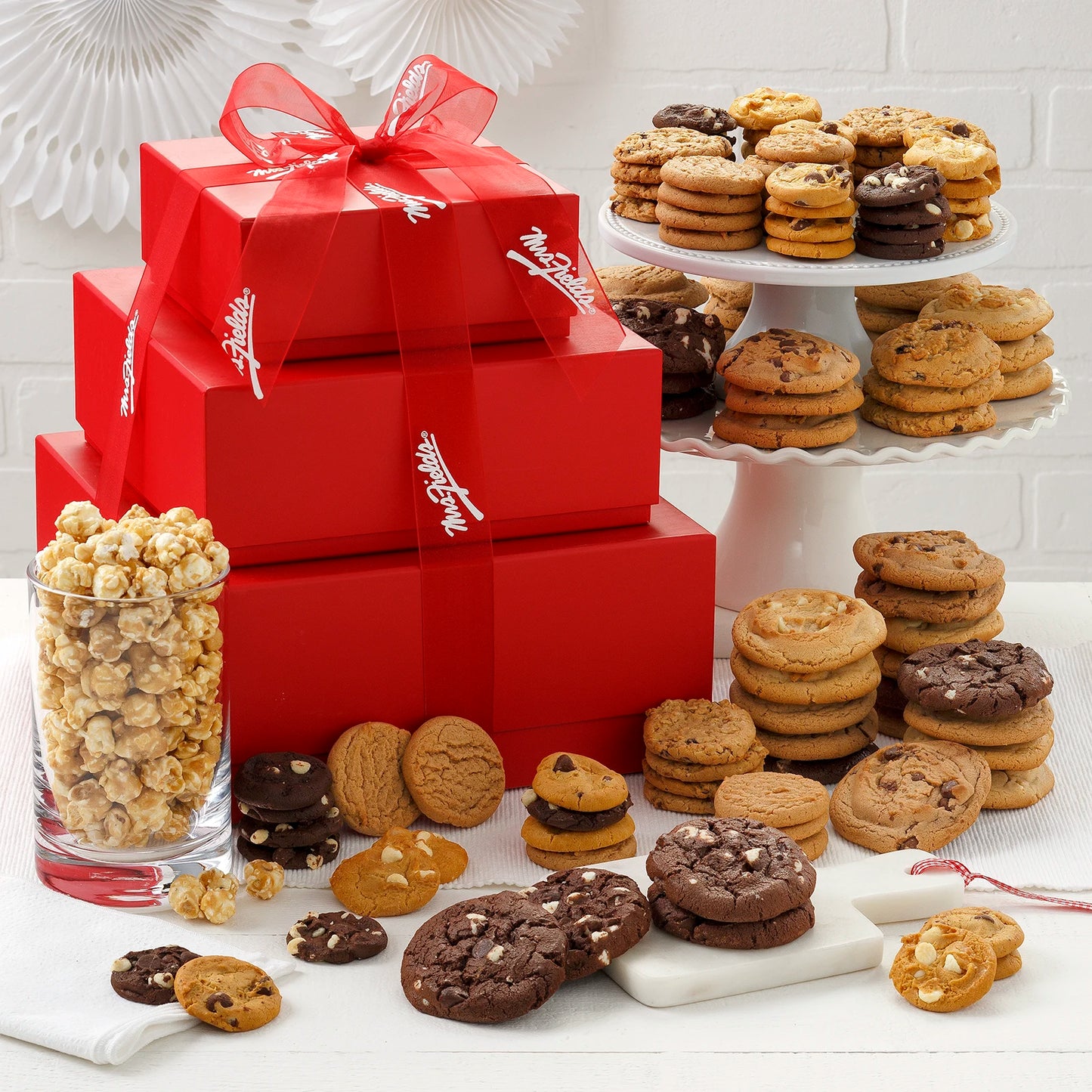 A stack of red boxes topped with a Mrs. Fields Box. These boxes come filled with Nibblers® Bite-Sized Cookies, original cookies and toffee nut popcorn