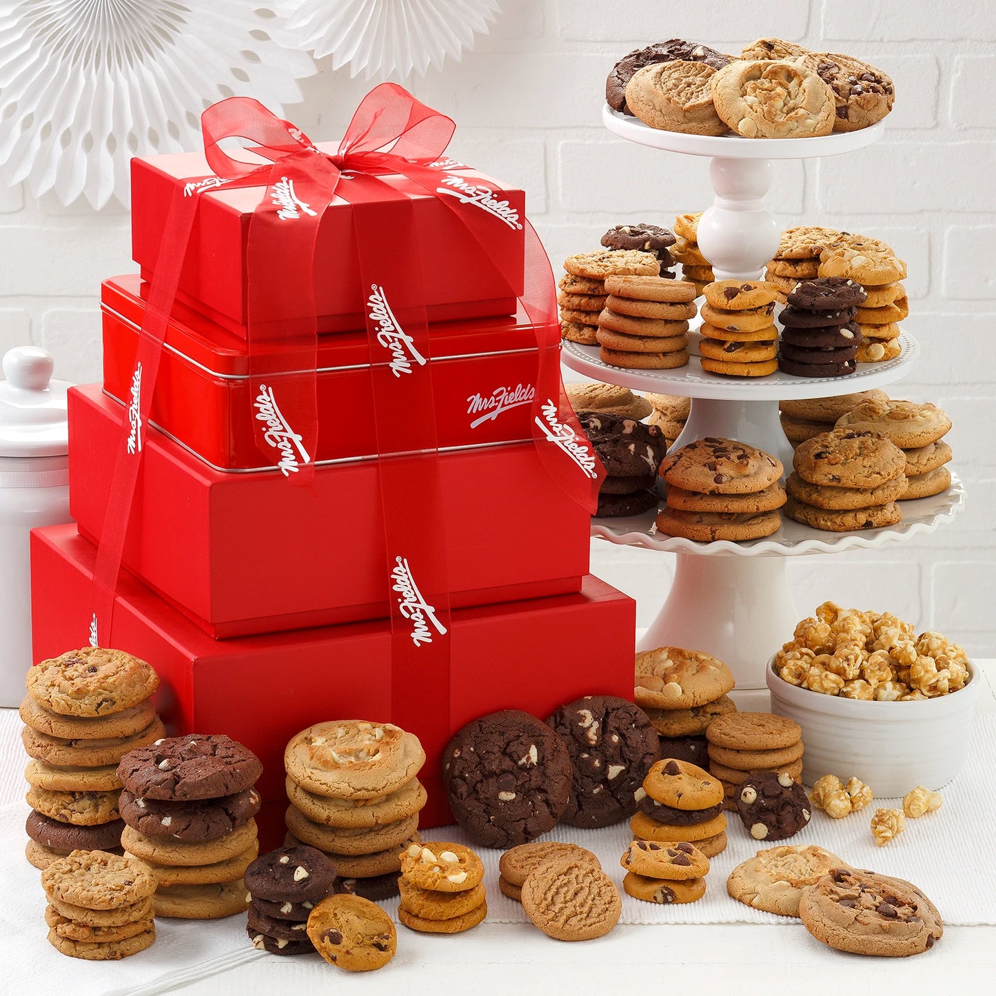 A stack of red boxes and a tin come filled with original cookies, Nibblers® Bite-Sized Cookies and toffee nut popcorn