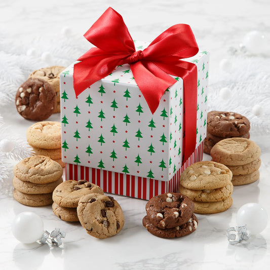 An adorable holiday themed mini cookie box with a pine tree print and tied with a red bow surrounded by Mrs. Fields Nibblers bite-sized cookies in five flavors including chocolate chip and white chocolate on a white surface with white Christmas ornaments.