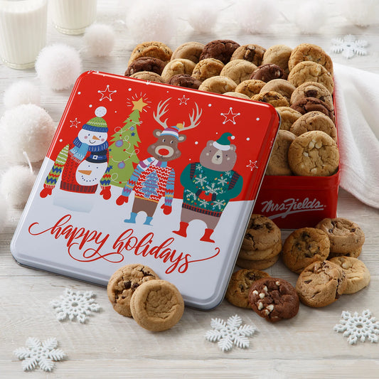 A cookie tin that says "Happy Holidays" on it with a snowman, a reindeer, and a bear all dressed in sweaters filled with Mrs. Fields Nibblers bite-sized cookies in five flavors including chocolate chip and oatmeal raisin on a white background with snowflake cutouts and a glass of milk.