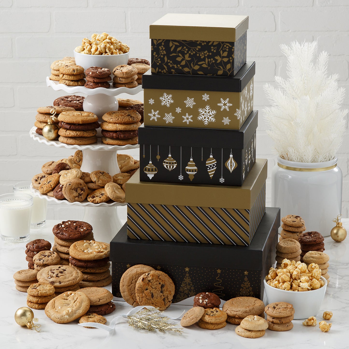 Five-tiered tower of black and gold holiday  boxes filled with Mrs. Fields original cookies and Nibblers bite-sized cookies as well as a generous helping of toffee nut popcorn on a white surface.