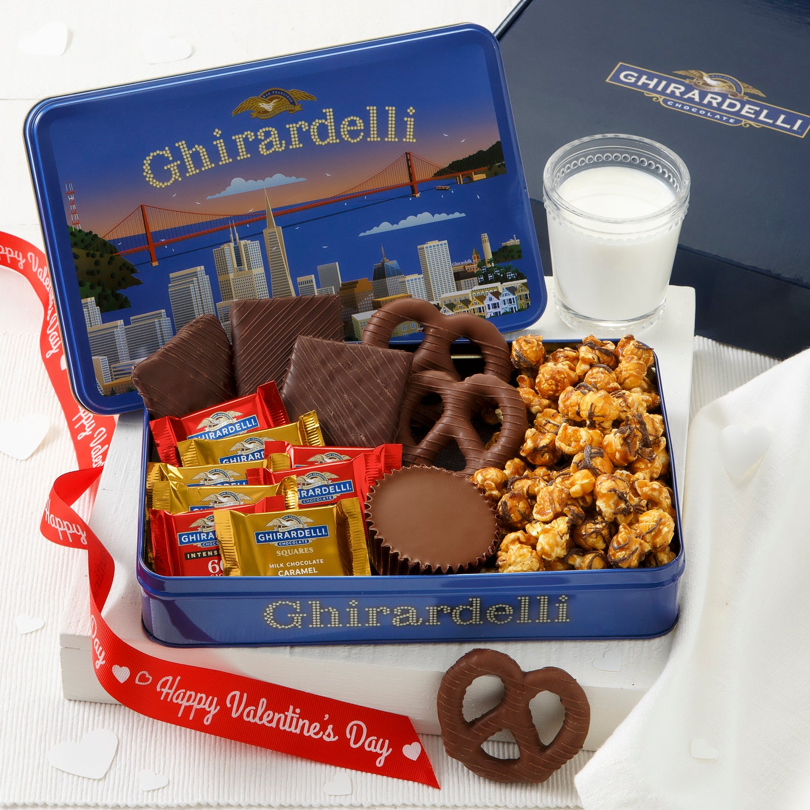 A blue Ghirardelli gift tin filed with an assortment of chocolates and treats