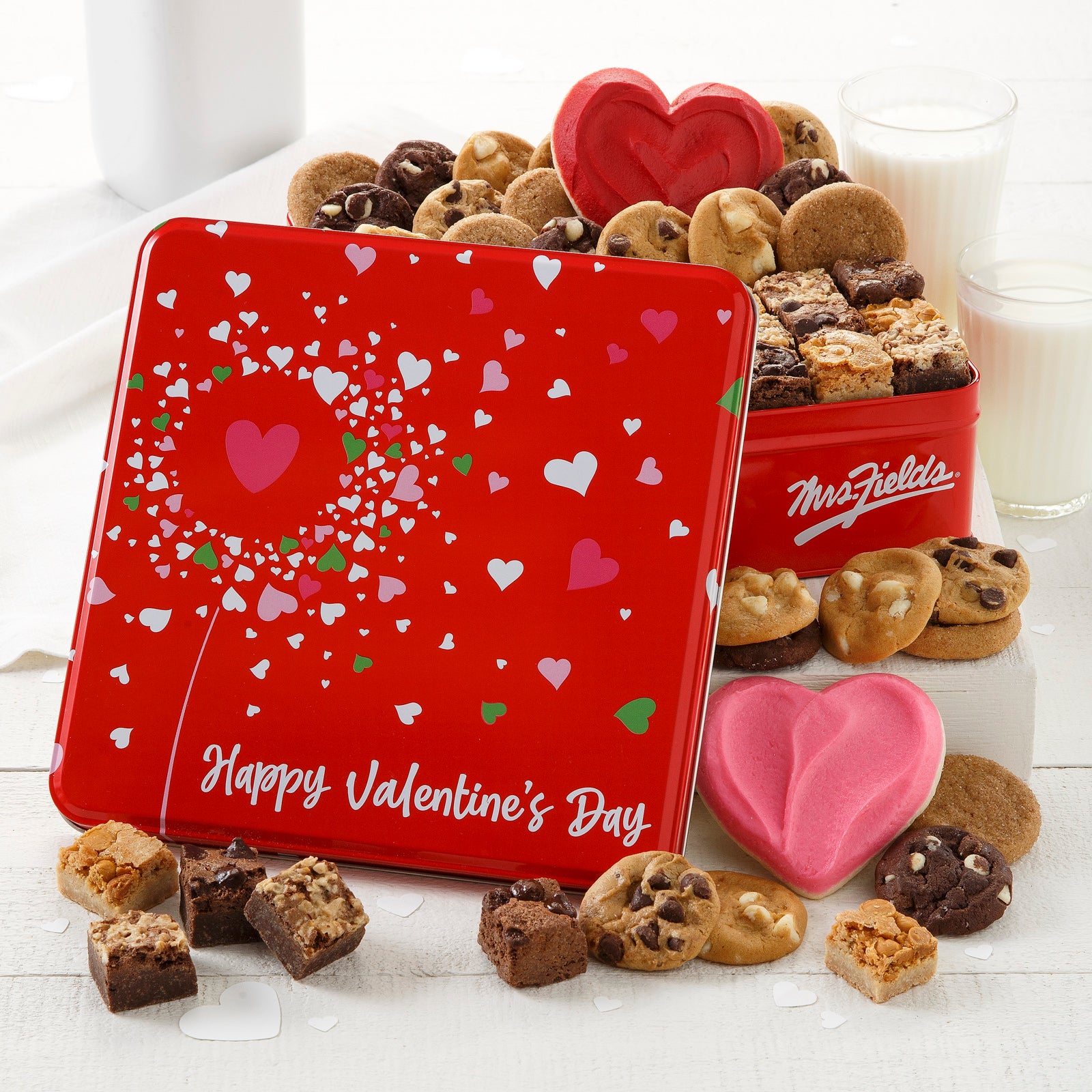 A red with hearts Valentine's Day tin filled with an assortment of nibblers, brownie bites, and frosted heart cookies