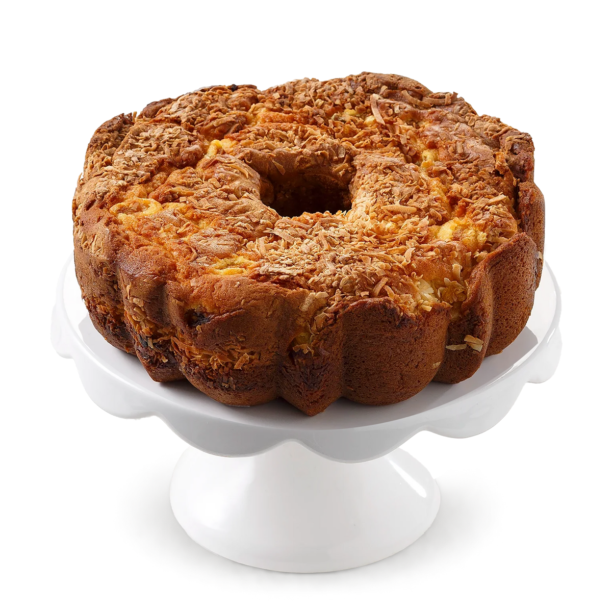 A large ring-shaped pineapple coconut cake topped with shredded coconut, displayed on a white scalloped cake stand.