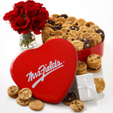 Mrs. Fields signature heart shaped tin filled with an assortment of Nibblers bite-sized cookies on a white surface with red roses